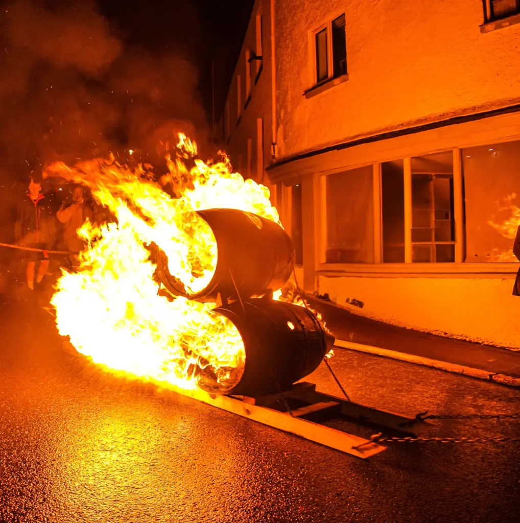 Two blazing tar barrels on a sledge being hauled through the street, with flames streaming behind