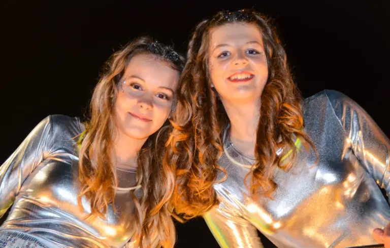 Two smiling girls in metallic silver outfits posing together on a float at night