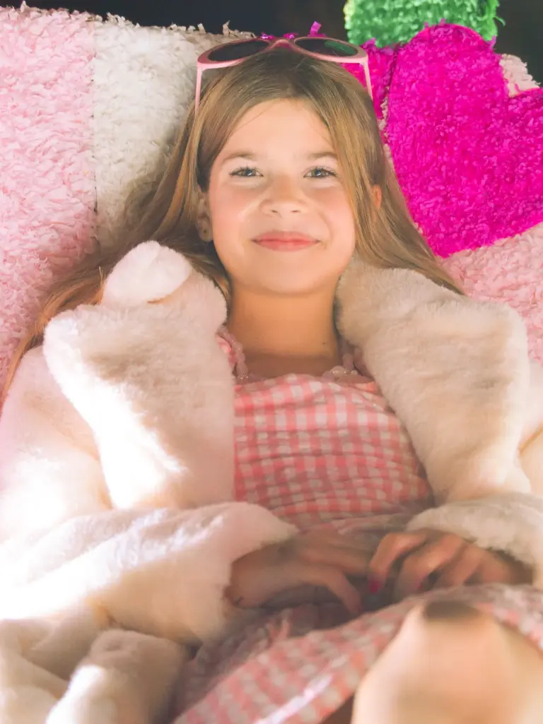 Girl in a pink gingham dress and fluffy white coat relaxing on a pink themed float