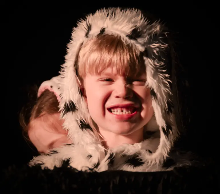 Child in a fluffy spotted dalmatian hood grinning widely in the dark