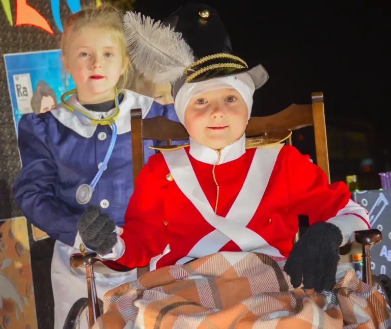 Child dressed as a Victorian nurse beside a child dressed as a redcoat soldier in a wheelchair under a tartan blanket