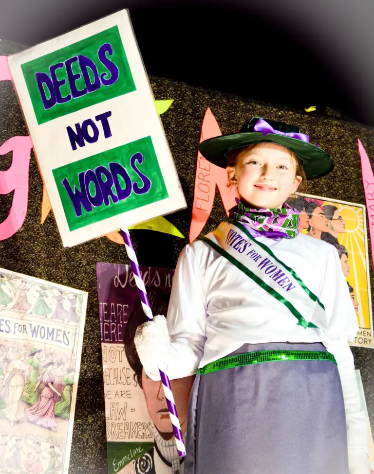 Girl dressed as a suffragette holding a Deeds Not Words placard on a Great Women themed float