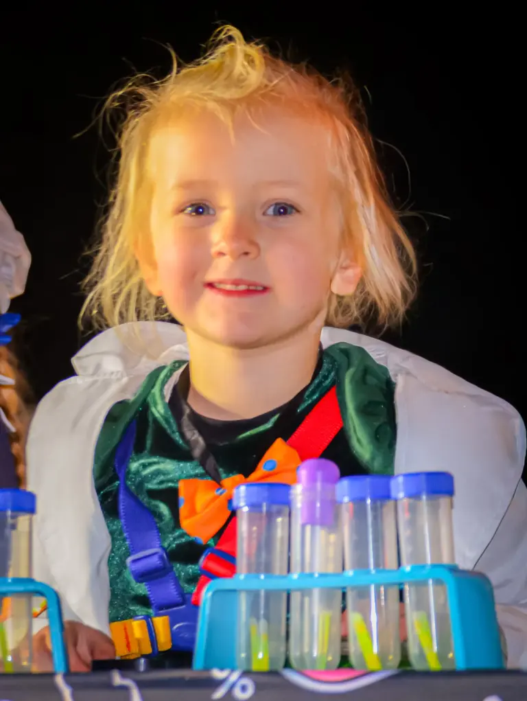 Small blonde child in a lab coat with test tubes, dressed as a scientist
