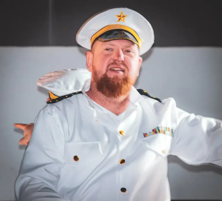 Bearded man in a white naval captain's uniform and cap smiling on a boat float