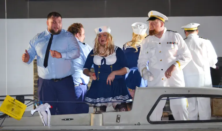 Group in Border Force shirts, sailor dresses and naval whites dancing on a boat float