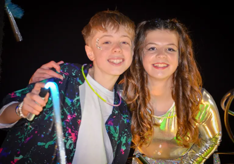 Boy and girl in glittery neon outfits smiling together at the night carnival