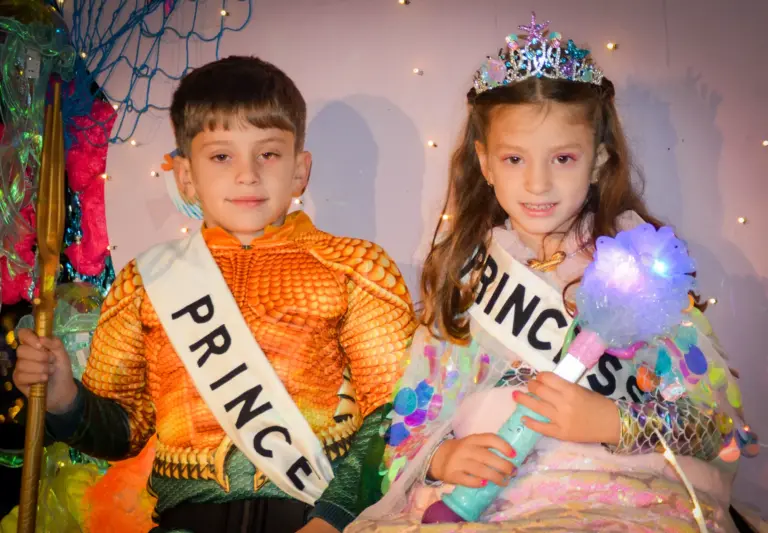 Young carnival prince dressed as Aquaman and princess in a tiara wearing their sashes