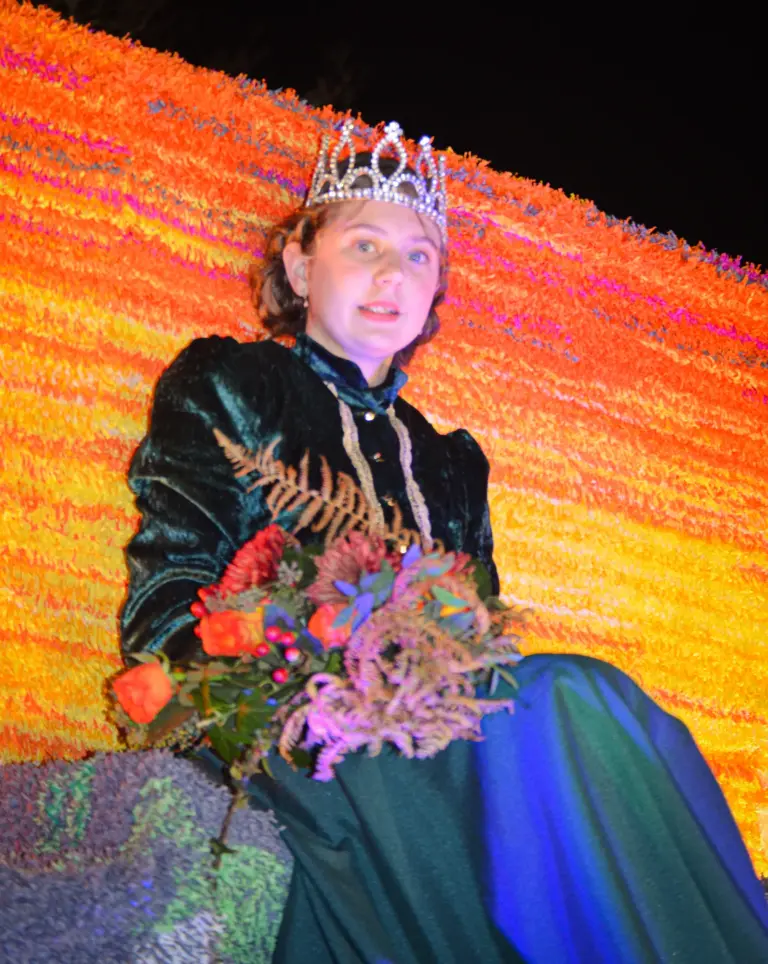 Girl in a tiara and green velvet gown holding a bouquet on an orange crepe-paper float