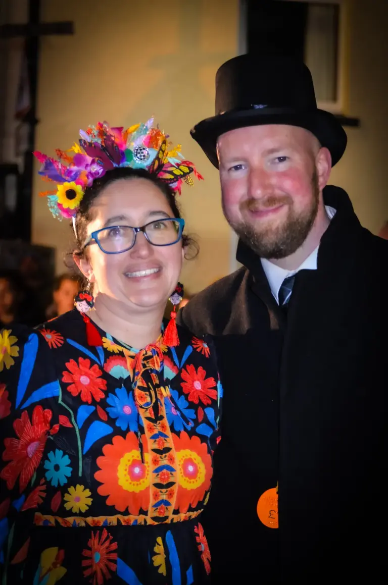 Woman in a flower crown and embroidered dress beside a man in a top hat at the evening carnival