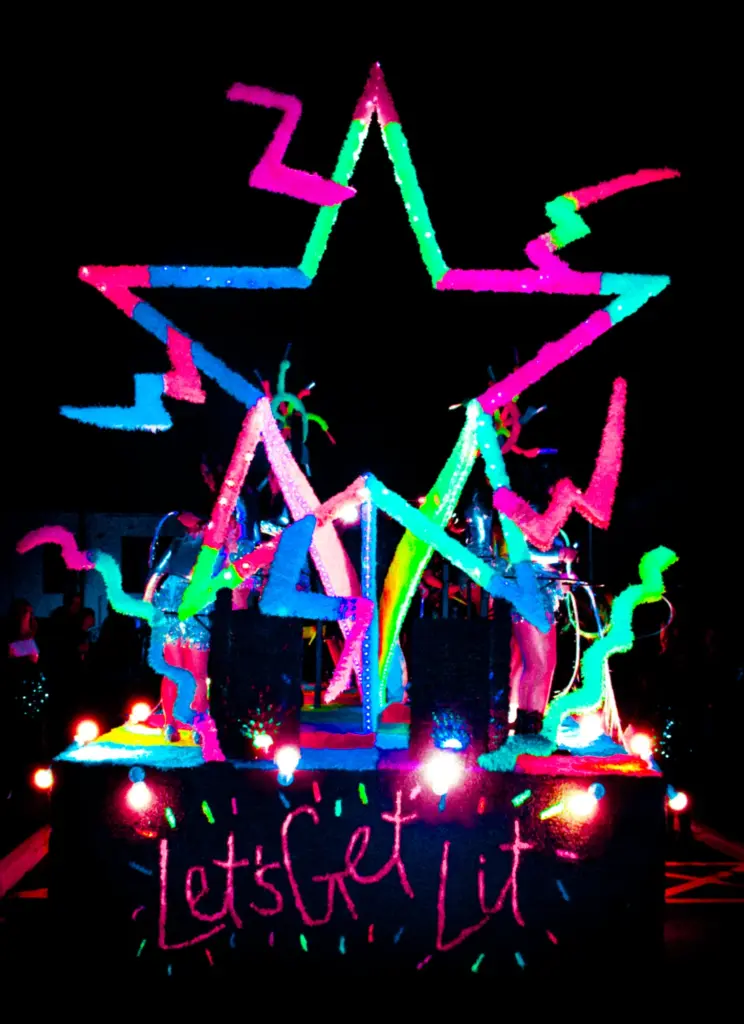 Neon crepe-paper star and lightning bolt float lit up against the night sky