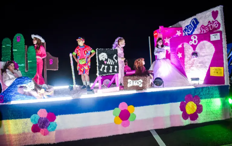 Wide view of the pink Barbie and Ken themed float with costumed riders lit up at night