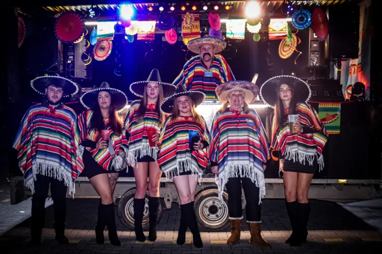 Group in sombreros and striped ponchos posing in front of a fiesta themed float