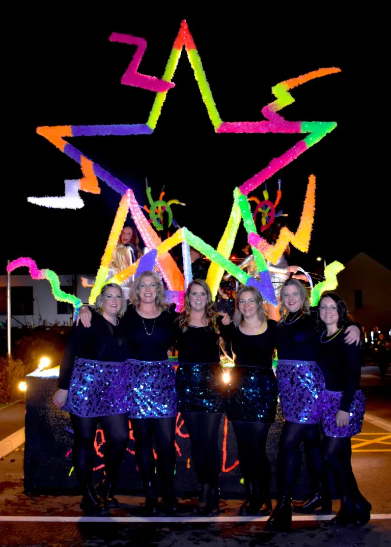 Women in sequin skirts in front of the neon star and lightning bolt float