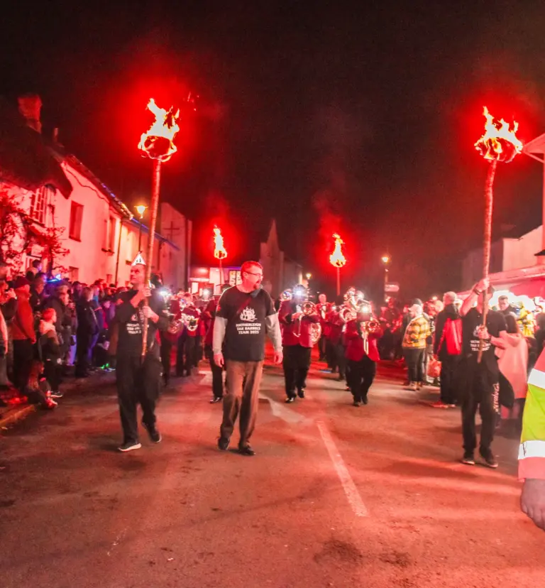 Torch bearers and marching band processing down the street under red light