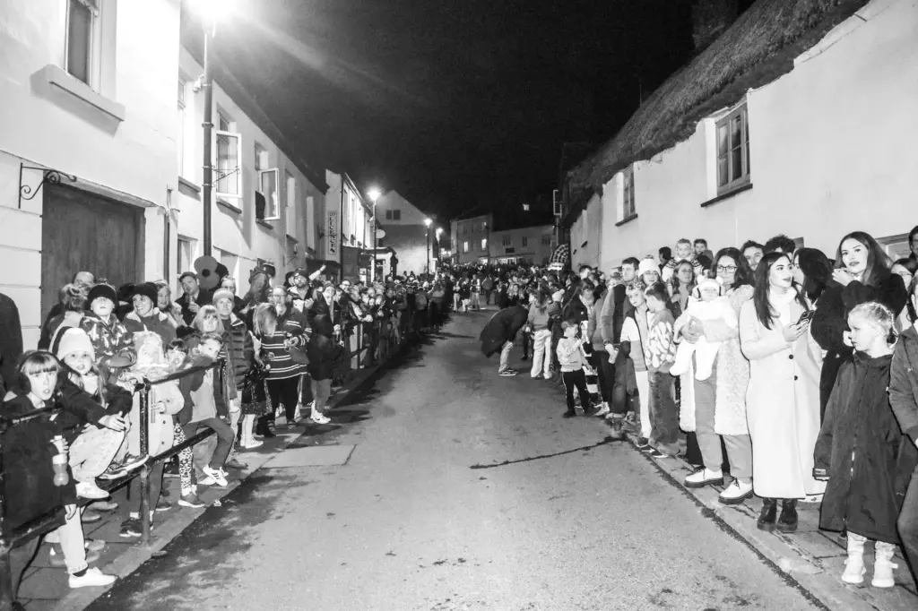 Black and white photo of crowds lining both sides of Hatherleigh's high street at night