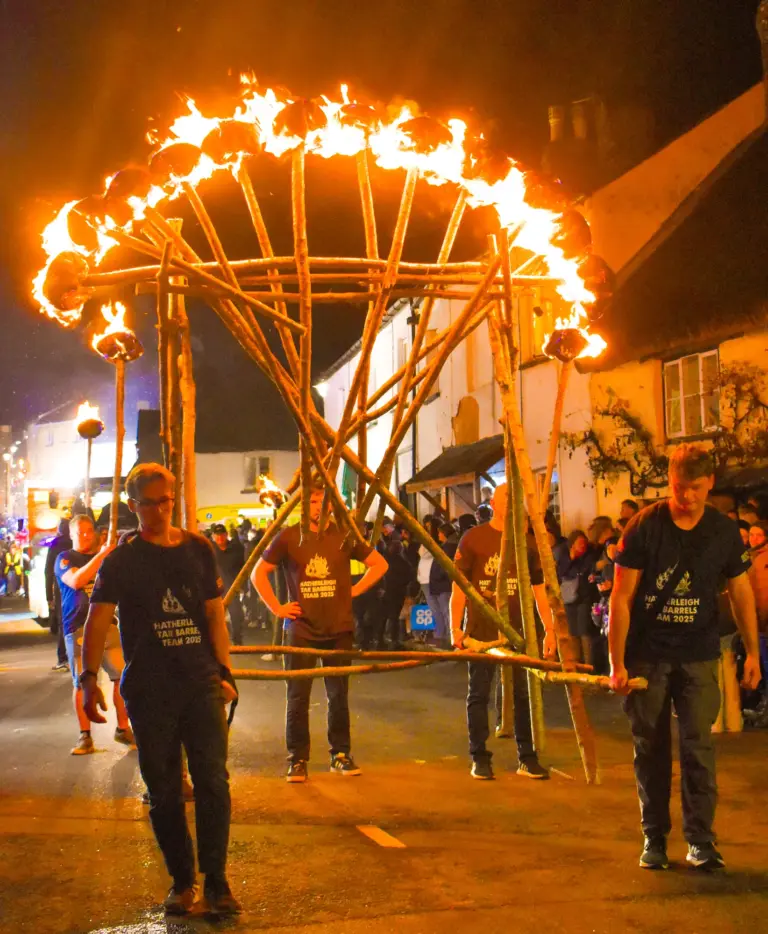 Men carrying a large flaming fire wheel frame through the street at night