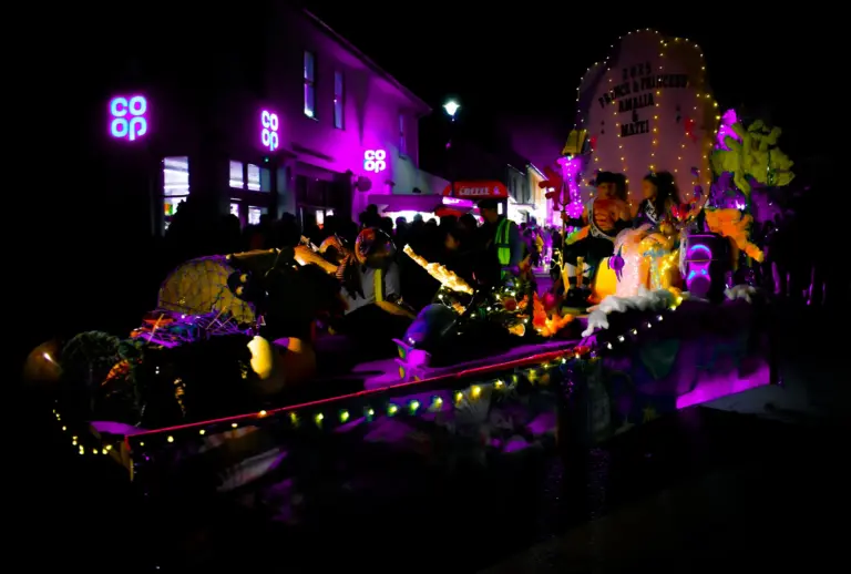 Float glowing purple and gold passing the Co-op on the high street at night