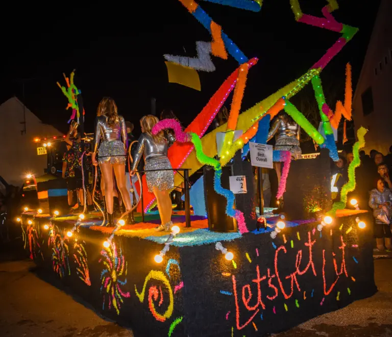 The neon Let's Get Lit float with silver-suited dancers in the procession