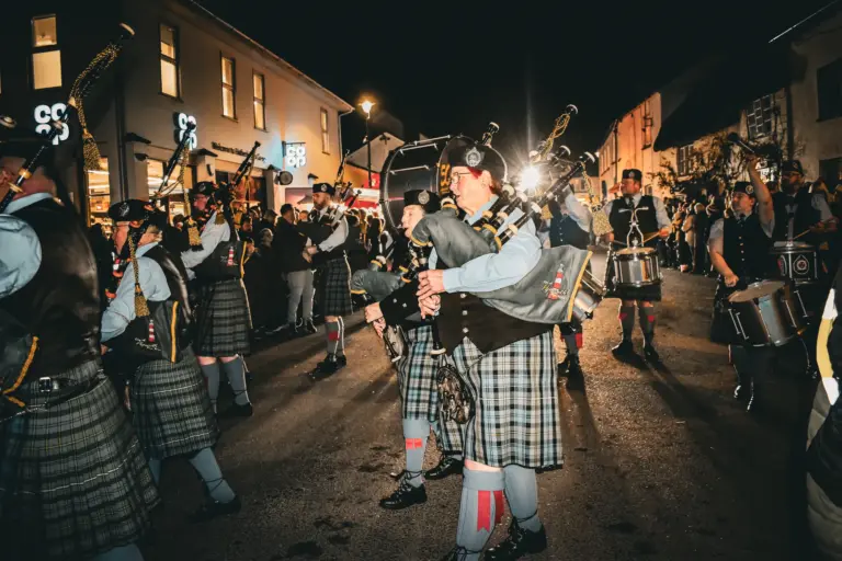 Pipe band in kilts playing bagpipes and drums along the high street