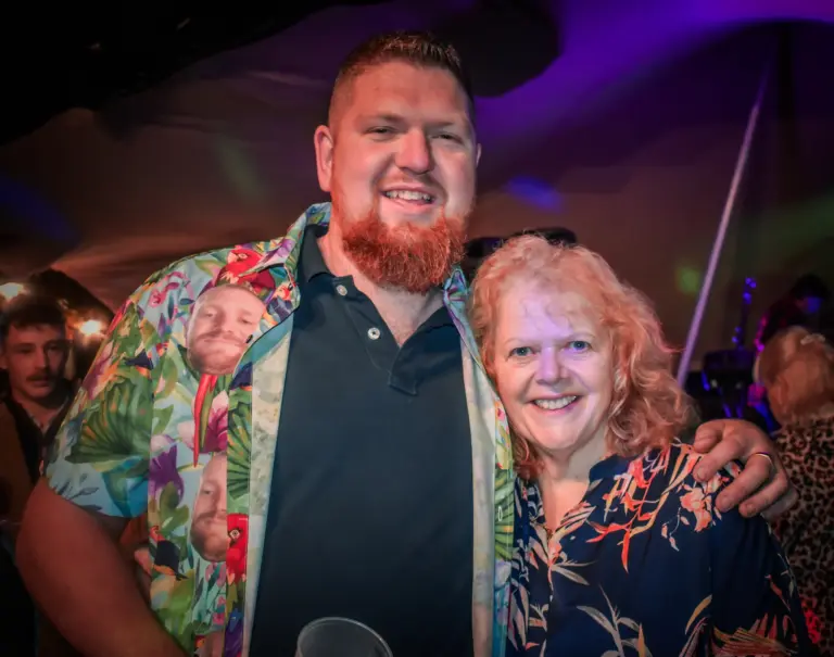 Bearded man in a tropical print shirt with his arm around a smiling woman at the Friday night party