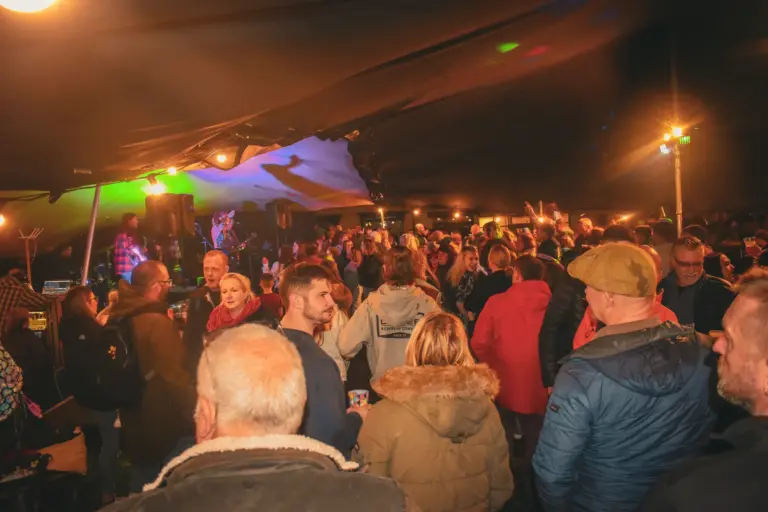 Crowd of people enjoying the music and drinks under a lit marquee on Friday evening