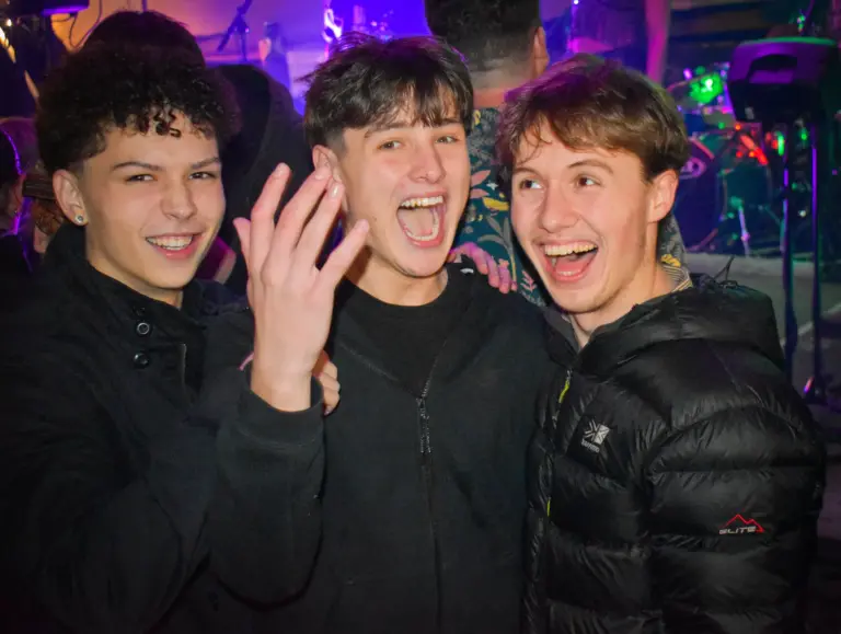 Three teenage boys cheering and laughing under purple stage lights