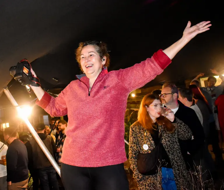 Woman in a pink jumper throwing her arms up in celebration at the Friday evening party