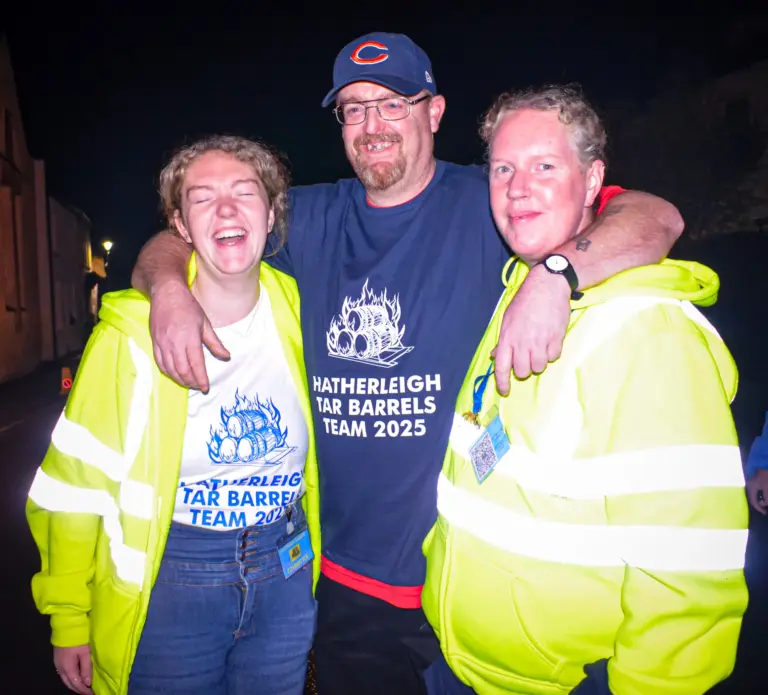 A Tar Barrels Team 2025 member with his arms around two marshals in hi-vis jackets