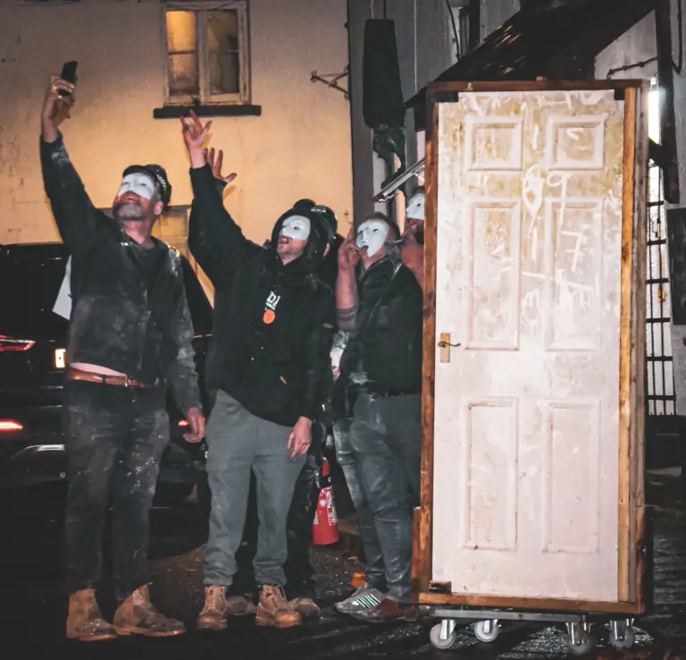 Black and white photo of masked tar barrel runners celebrating beside a wooden door