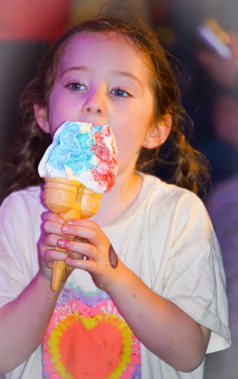 Young girl licking a rainbow ice cream cone at the carnival