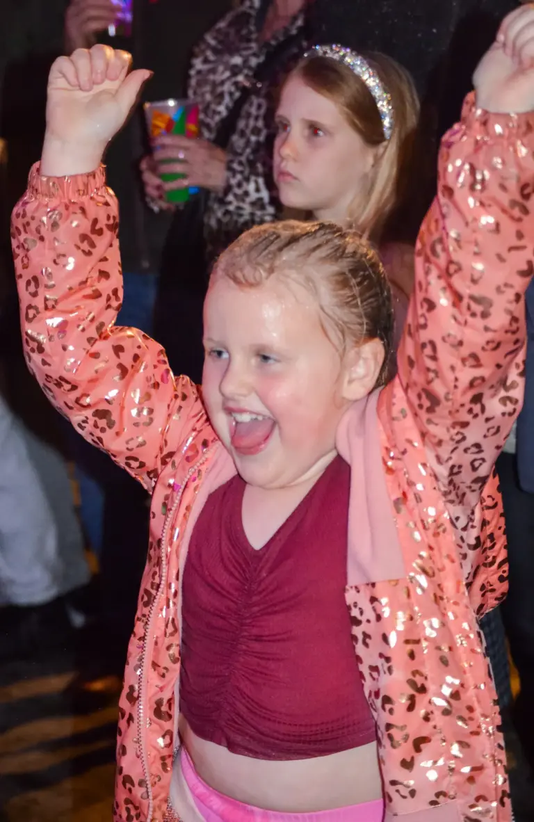 Little girl in a sparkly jacket cheering with her arms in the air