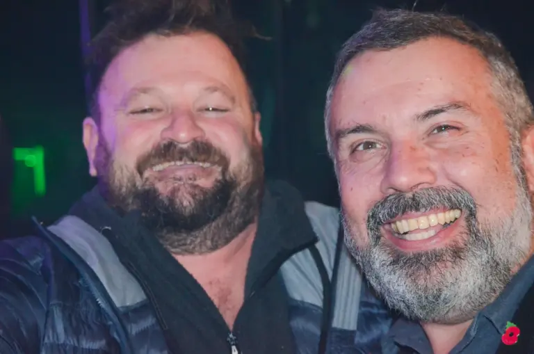 Two bearded men grinning for a selfie-style photo on carnival night
