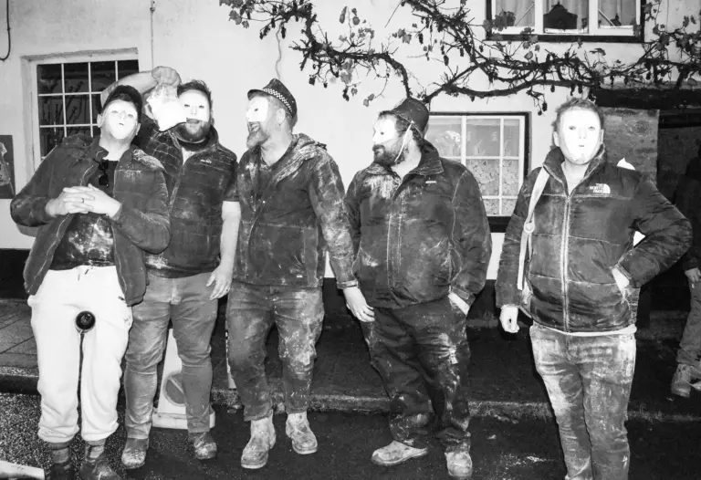 Black and white photo of masked tar barrel runners in soot-covered clothes