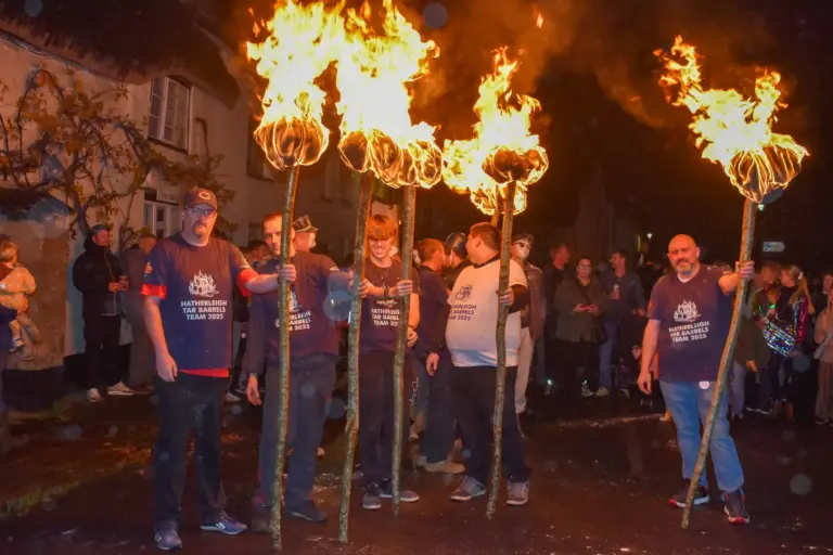 Tar barrel team members holding tall flaming torches in the street at night
