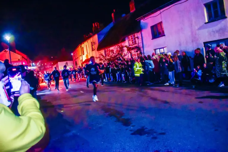 Tar barrel runners racing down the street past crowds lit with blue and red light