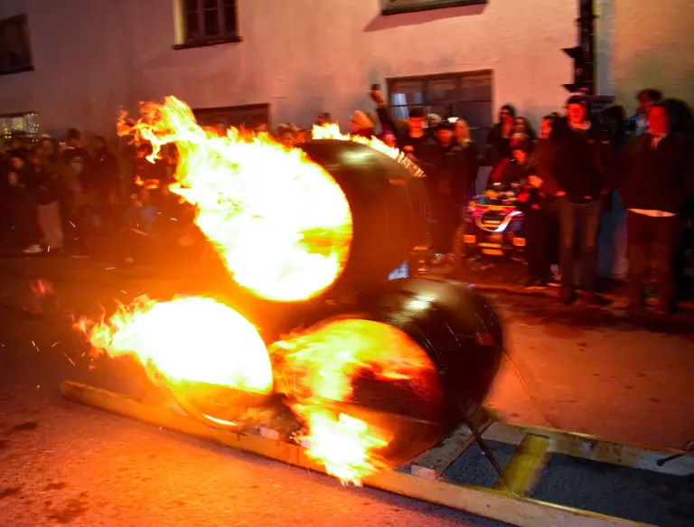 Blazing tar barrels rushing past on a wooden sledge as cheering crowds line the street