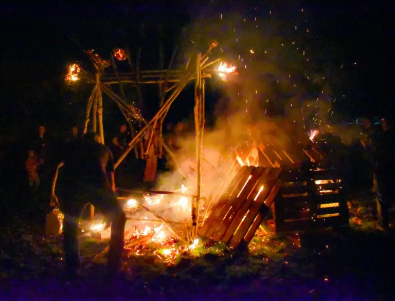 Bonfire blazing beneath a wooden frame with sparks flying into the night sky