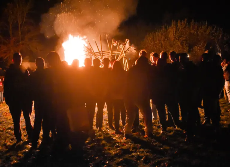 Crowd silhouetted against the bonfire as smoke rises into the night