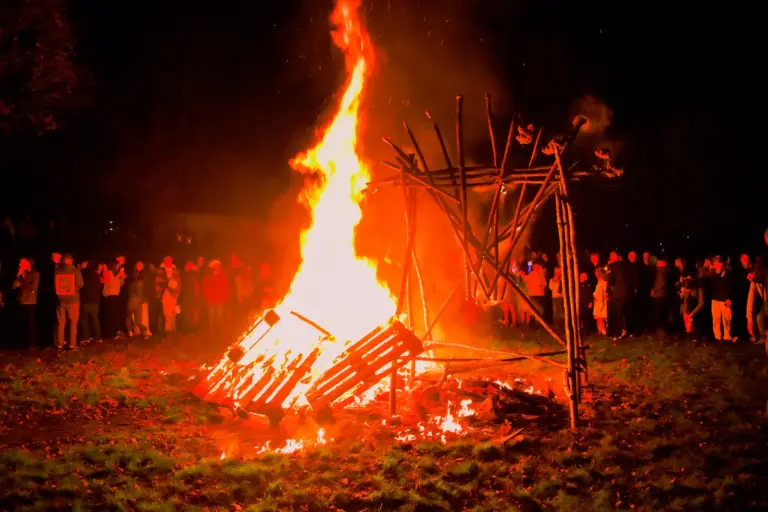 Tall flames rising from the bonfire with the crowd watching in a ring