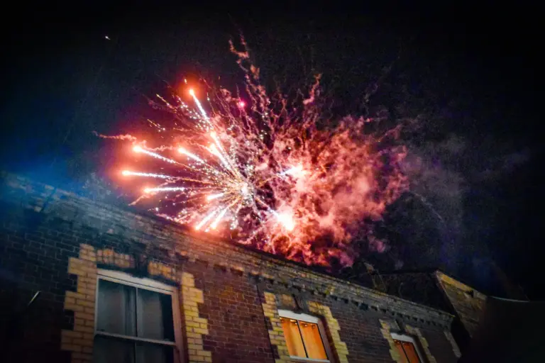 Pink fireworks bursting over a brick building at night