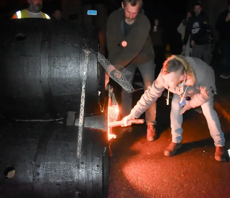 Volunteer lighting the tar barrels with a flaming torch in the dark