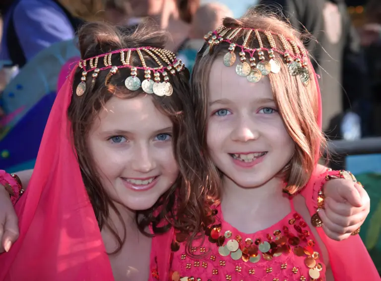 Two smiling girls in pink costumes with gold coin headdresses
