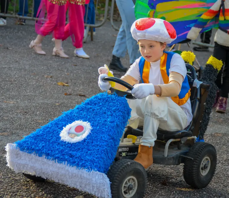 Child dressed as a mushroom character driving a blue crepe-paper go-kart