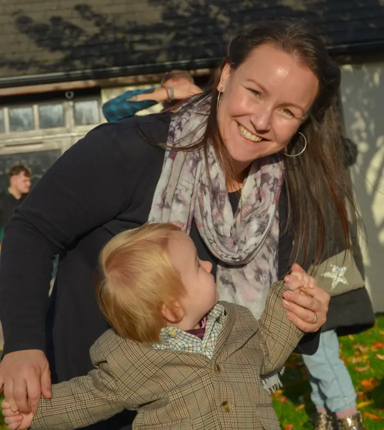Smiling woman holding hands with a toddler in a tweed jacket at the afternoon parade