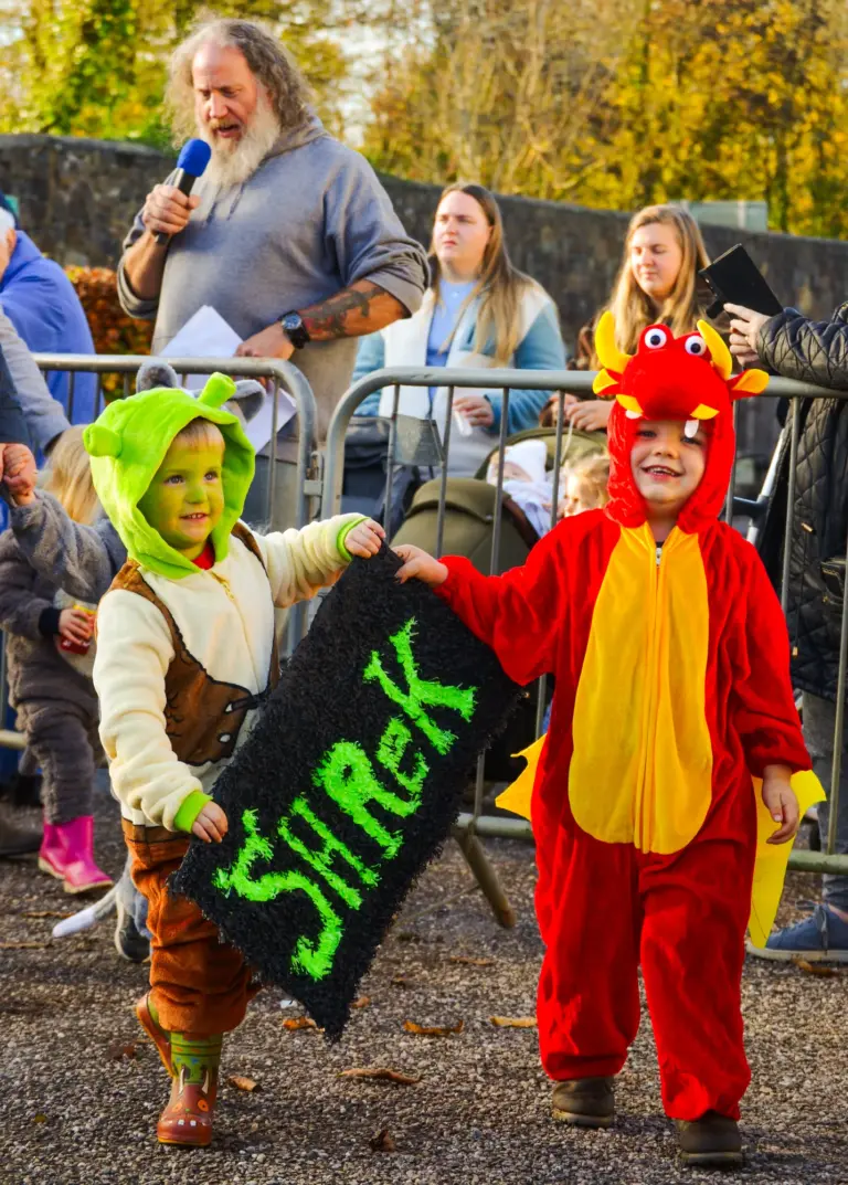 Children in dragon and ogre costumes carrying a Shrek sign past the judges