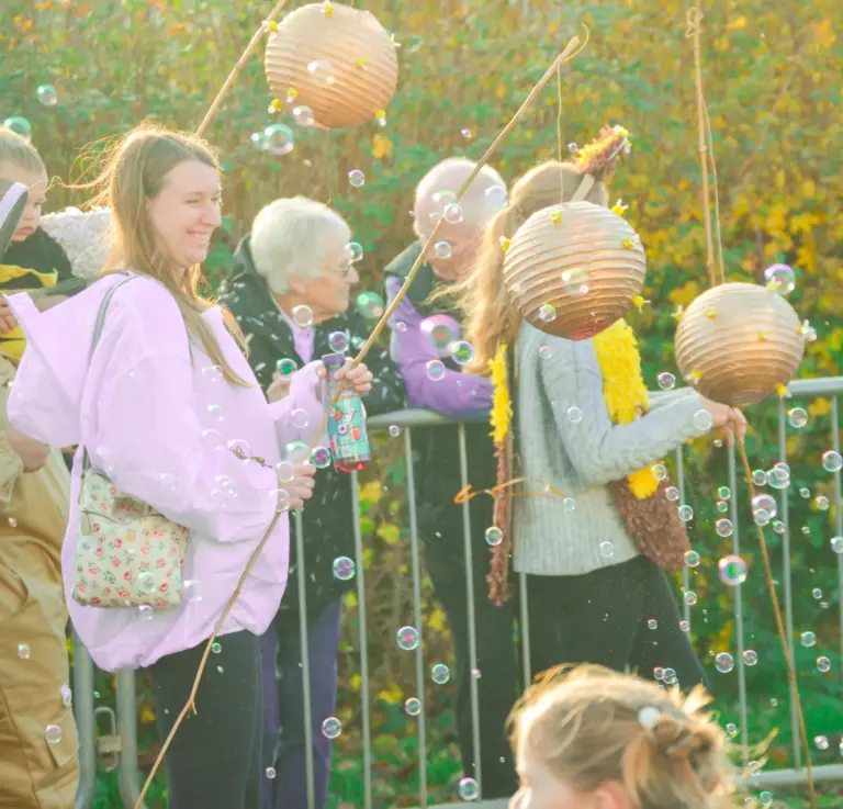 Bubbles floating around spectators holding paper lanterns in the autumn sunshine