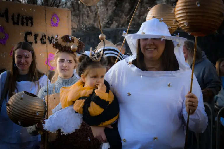 Woman in a beekeeper suit with a baby dressed as a bee and paper lantern hives