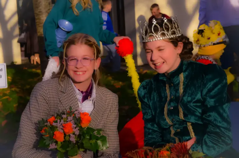 Girl in a crown and velvet gown beside a girl holding a bouquet of flowers