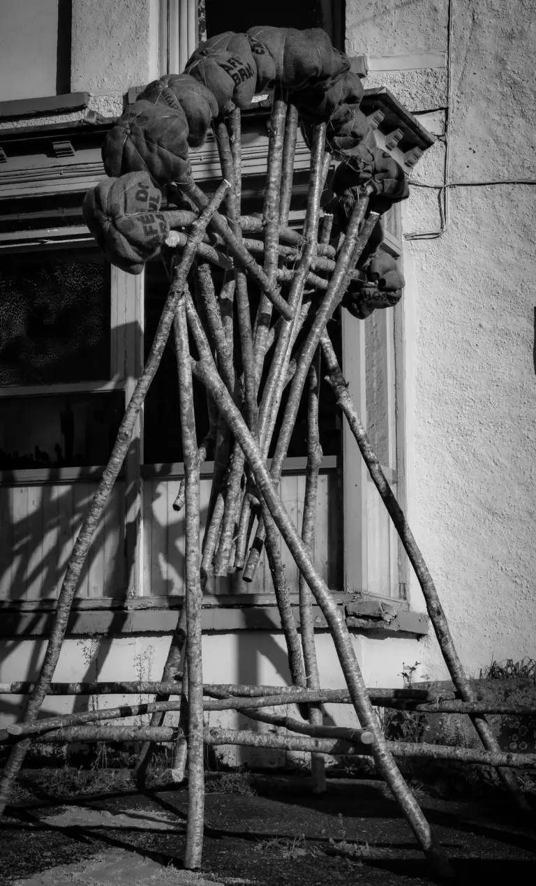 Black and white photo of the wooden bonfire frame leaning against a building