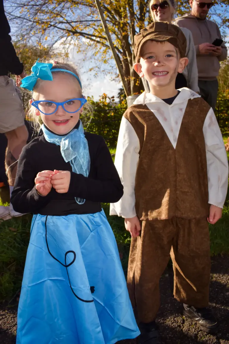 Girl in a blue poodle skirt and glasses beside a boy in a waistcoat and flat cap